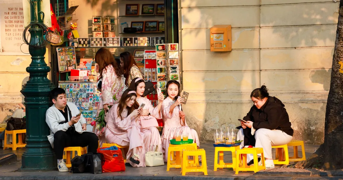 Hanoi street scene: locals on yellow stools using smartphones, reflecting app localization services.