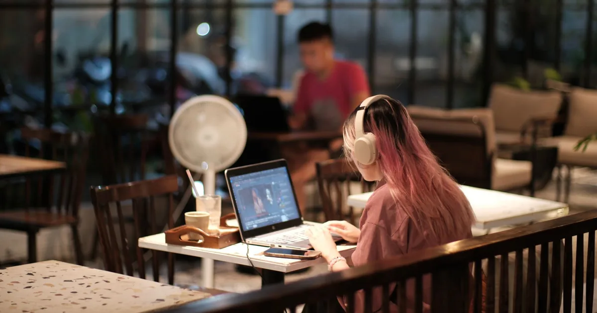 Woman in café edits video on laptop, showing human post-editing's value over automatic.