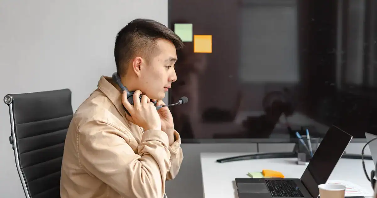 Man working with laptop in office setting, wearing a headset for an online meeting. - FAS Localize