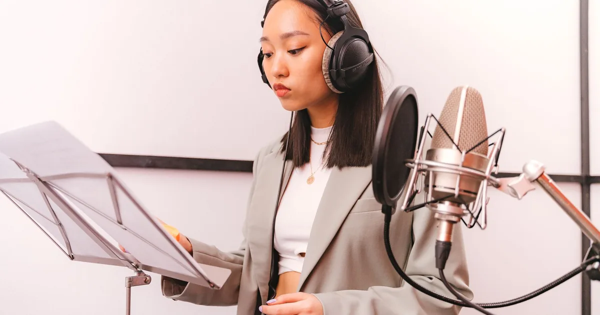 Asian woman in studio booth recording elearning voice over services with microphone.
