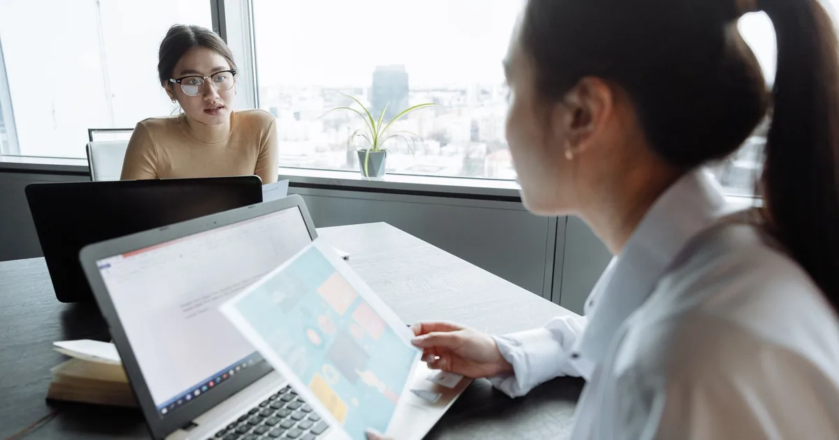 Businesswomen review localization project on laptops, discussing ideas in a modern office.