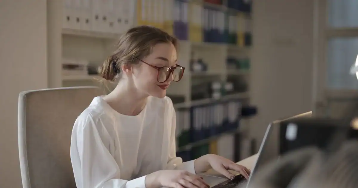 A professional woman concentrating on her laptop at a modern office desk. - FAS Localize
