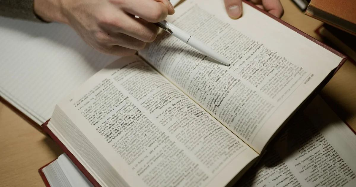 Hand with pen studying open book, exploring translation theories.