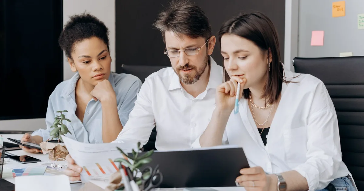 Coworkers discuss MTPE prices while collaborating at a modern office desk.