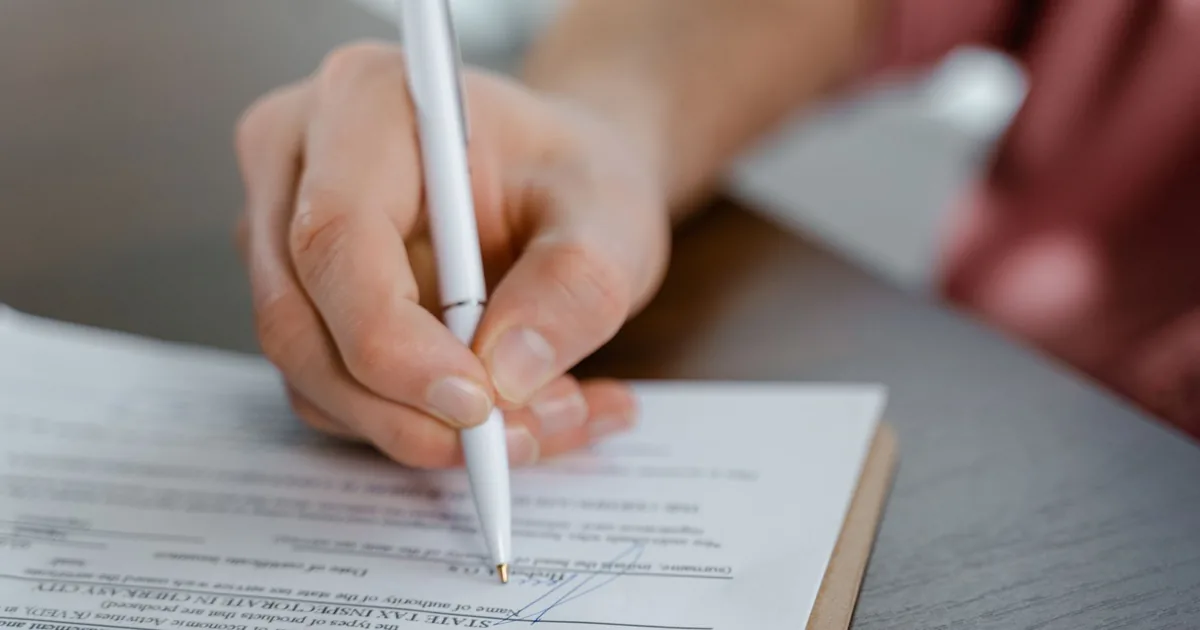 Detailed view of a hand writing a signature on an official document with a ballpoint pen. - FAS Loca