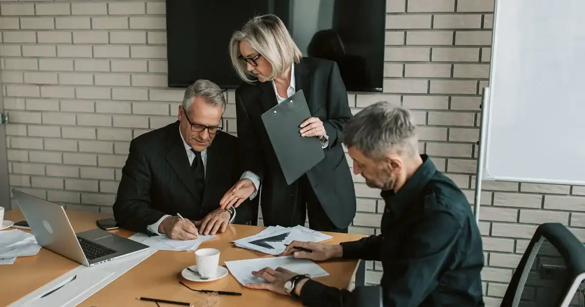 Three mature professionals in a business meeting discussing and signing documents in an office setti