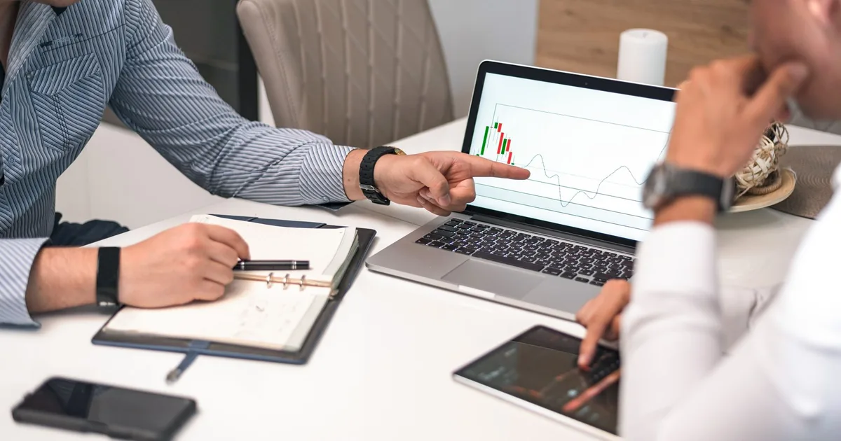 Businessmen analyze charts on laptop & tablet, reflecting Übersetzungsbüro MTPE criteria.