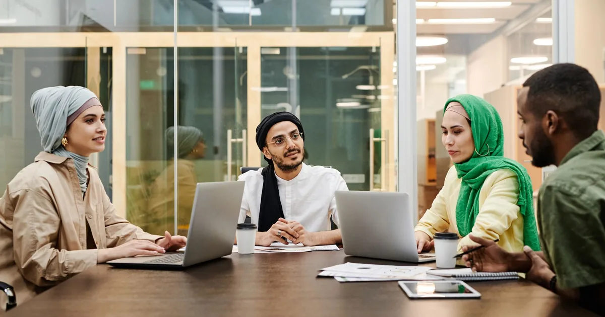 A diverse group discussing ideas in a modern office setting, using laptops and tablets. - FAS Locali