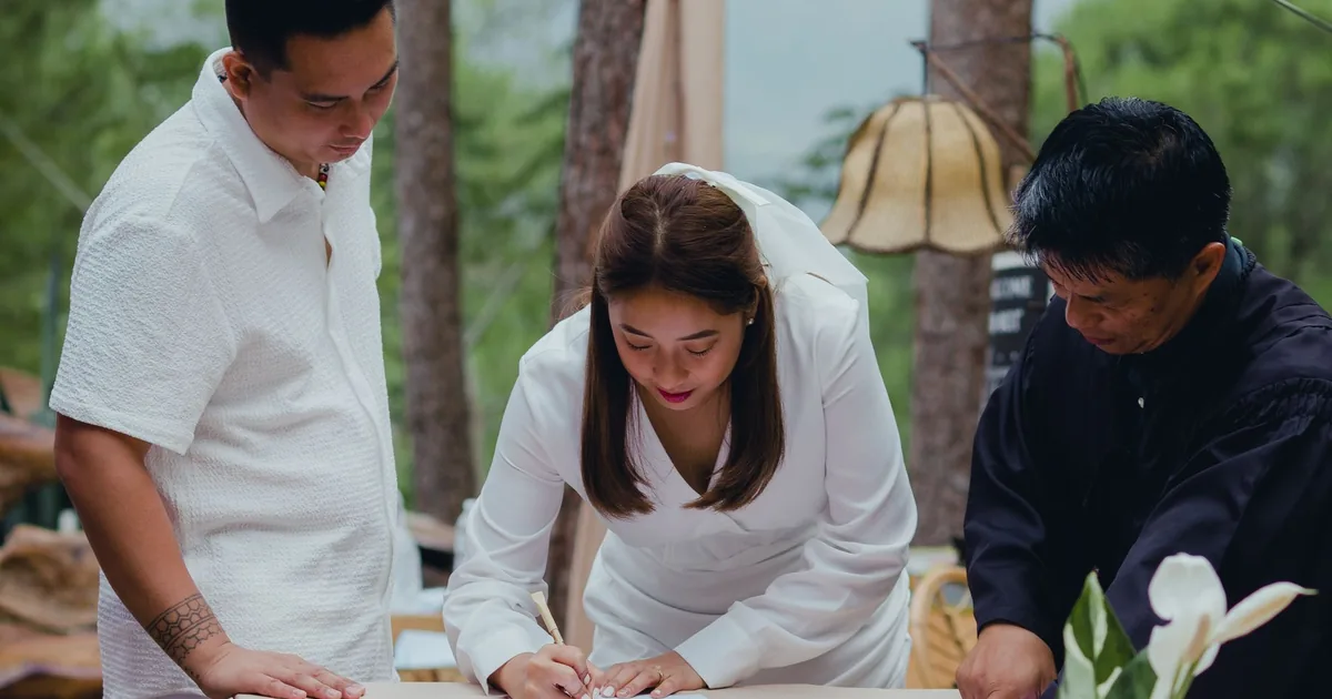 Bride signs marriage certificate; family looks on. Learn to certify Vietnamese marriage certificate