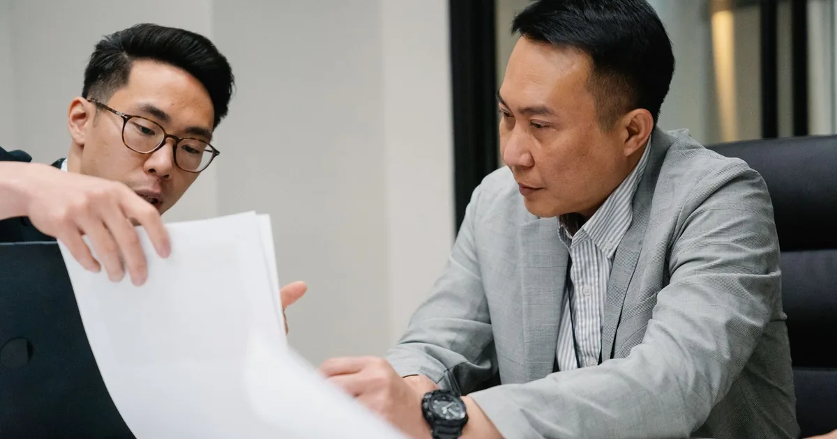 Two men discuss notarized vs certified Vietnamese translation in a modern office.